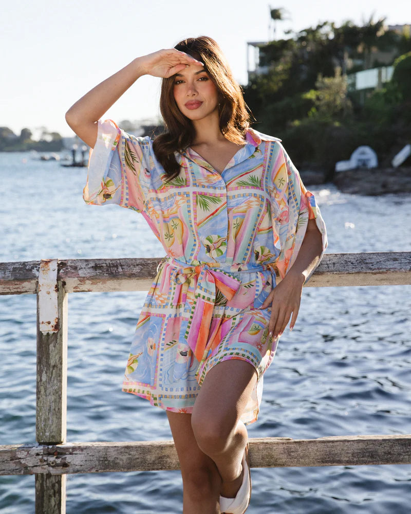 Woman in a colorful dress standing by a waterfront with a scenic background