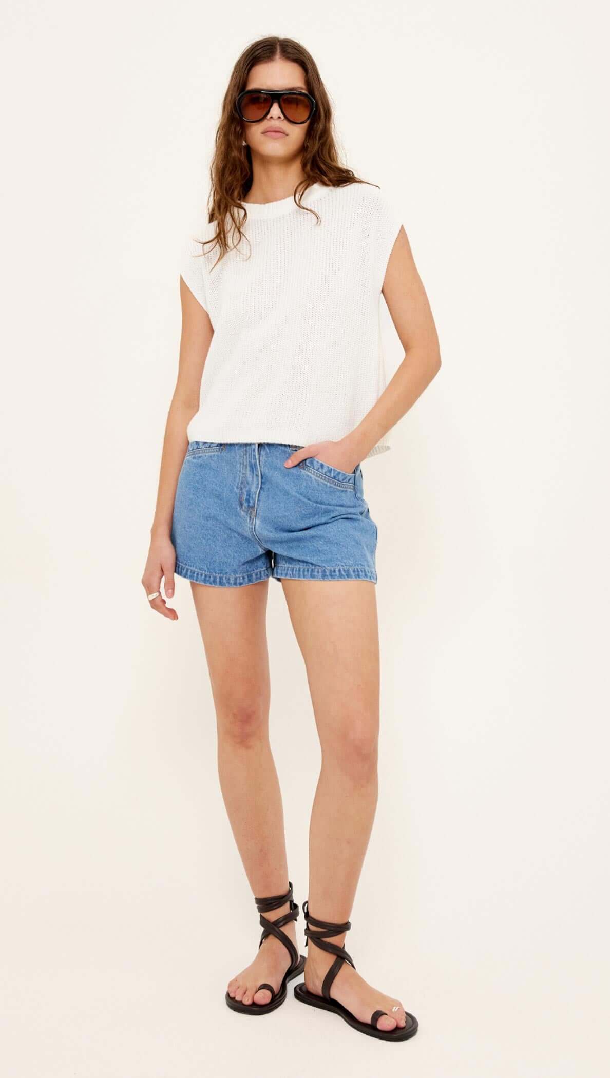 Woman wearing a white sleeveless top and blue denim shorts on a white background