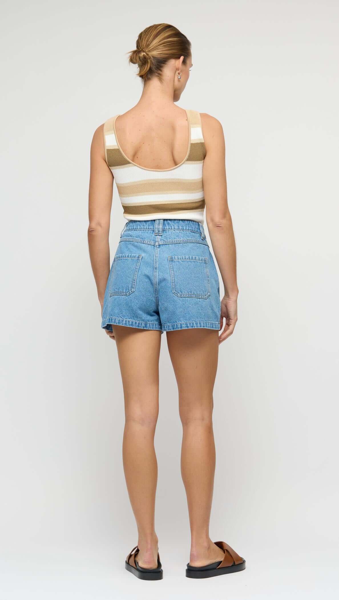 Woman wearing a striped tank top and denim shorts on a plain background