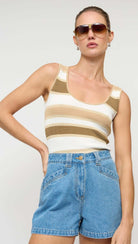 Woman wearing a striped tank top and denim shorts with sunglasses on a plain background