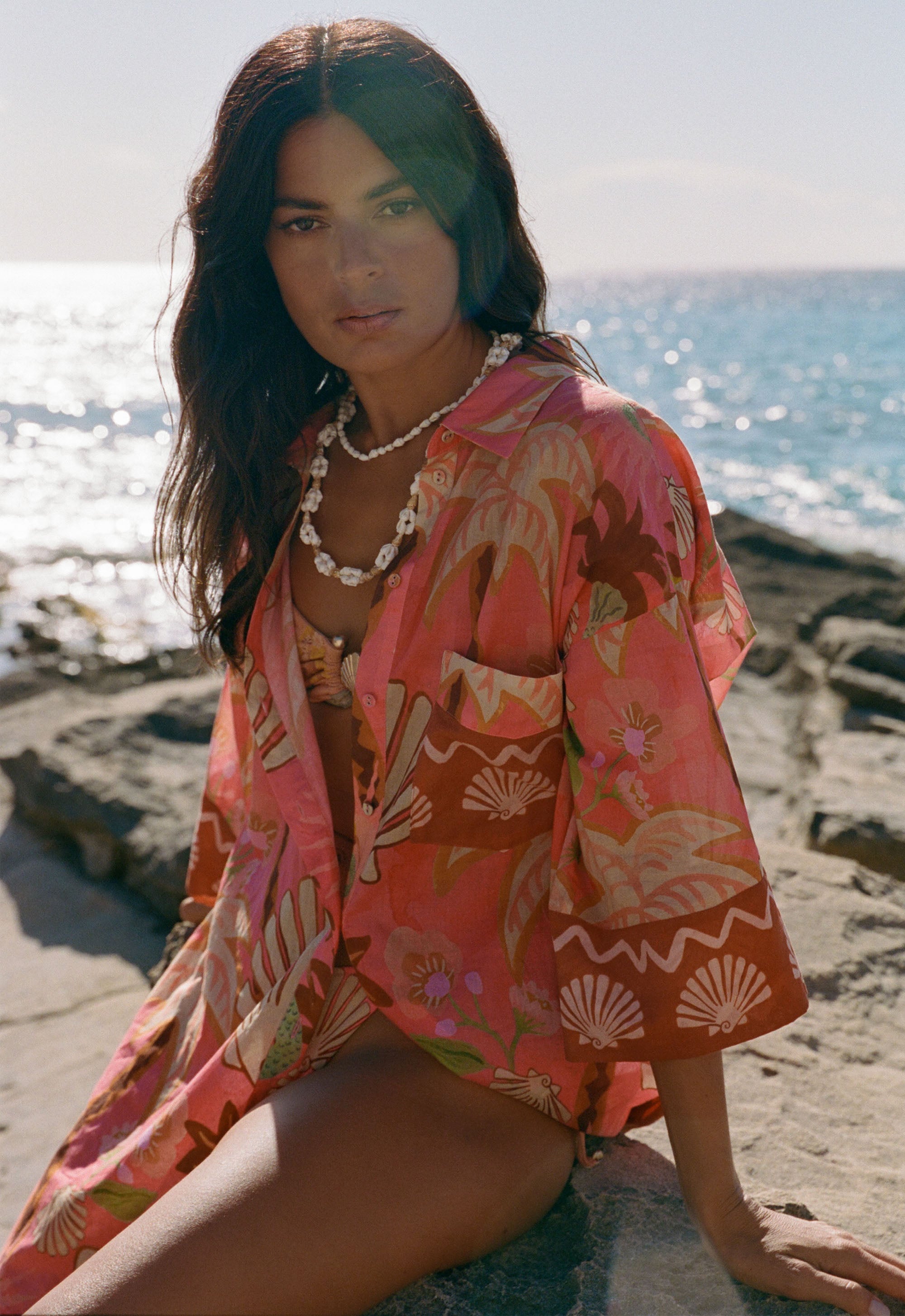Woman in a pink floral kimono sitting on a beach with ocean in the background