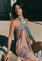 Woman wearing a colorful floral dress sitting on a stone surface.