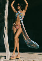 Woman in a colorful bikini and sarong standing against a dark background