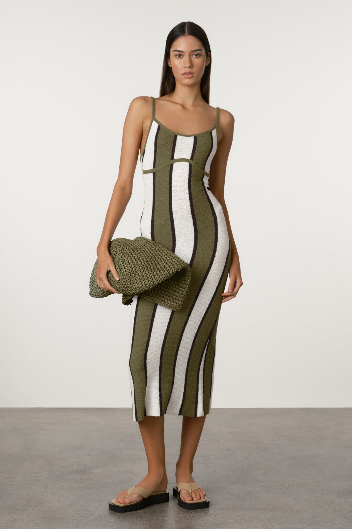 Woman wearing a green and white striped dress holding a matching clutch against a plain background