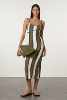 Woman wearing a green and white striped dress holding a matching clutch against a plain background