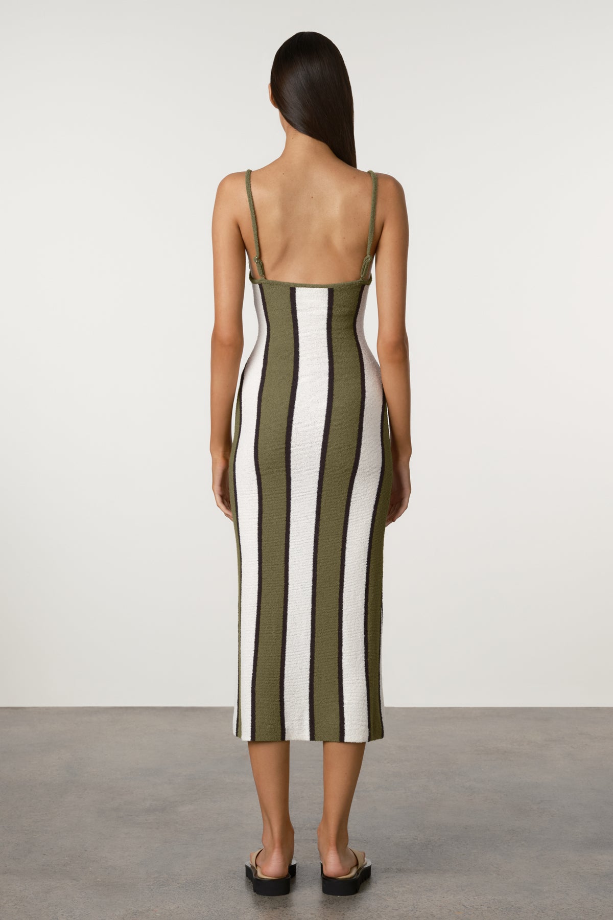 Woman wearing a striped dress with green, white, and black vertical stripes on a plain background