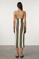 Woman wearing a striped dress with green, white, and black vertical stripes on a plain background