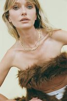 Woman wearing a fur garment and gold necklace against a plain background
