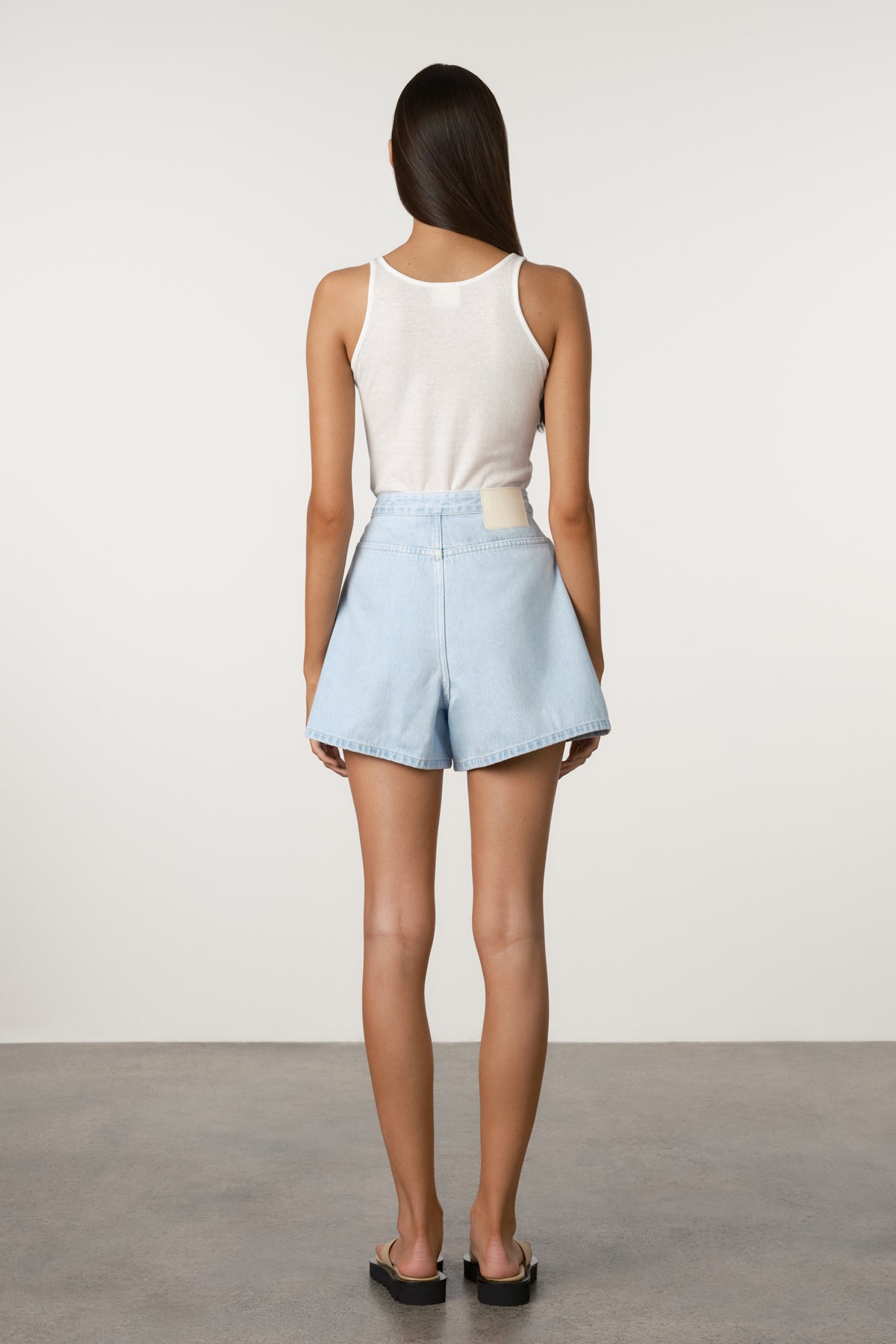 Person wearing a white sleeveless top and light blue shorts against a plain background