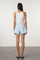 Person wearing a white sleeveless top and light blue shorts against a plain background