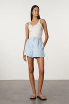 Woman wearing a white tank top and light blue shorts against a plain background