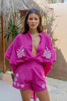 Woman wearing a bright pink outfit with white patterns in a tropical setting