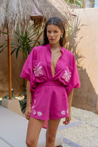 Woman wearing a bright pink outfit with floral patterns in an outdoor setting.