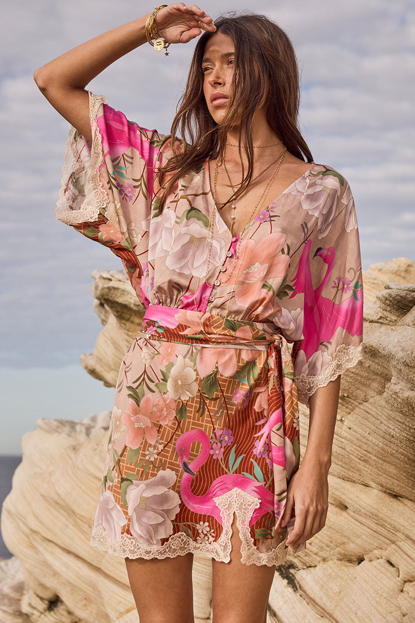 Woman wearing a floral and flamingo-patterned dress on a rocky beach.