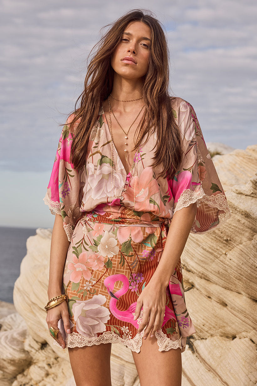 Woman in a floral dress standing on a rocky beach with ocean view