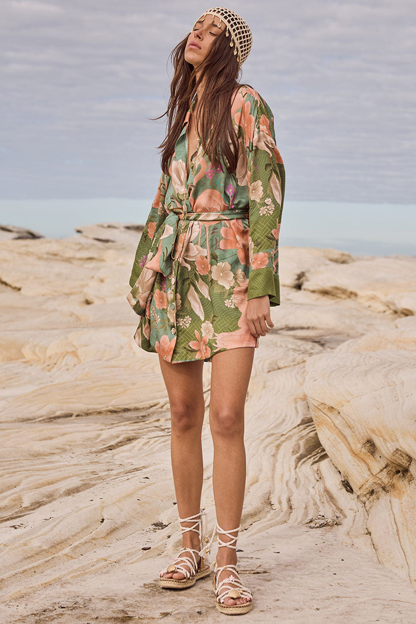 Woman in a floral dress standing on rocky beach with ocean view