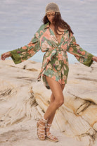 Woman in a floral dress standing on a rocky beach with ocean in the background