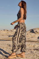 Woman in a patterned outfit standing on rocky terrain with a clear sky.