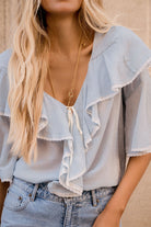 Light blue blouse with ruffled details and denim jeans worn by a person.