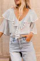 Woman wearing a light blue ruffled blouse and jeans against a beige wall.