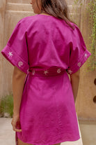 Person wearing a pink dress with star patterns against a beige wall.