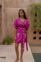 Woman wearing a pink dress with palm tree design in an outdoor setting.