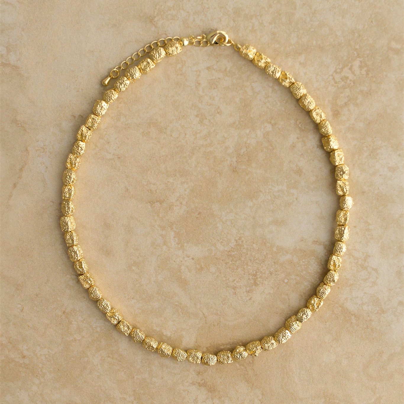 Gold necklace on a beige stone surface