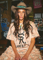 Woman wearing a cowboy hat and patterned outfit in a room with posters and decor.