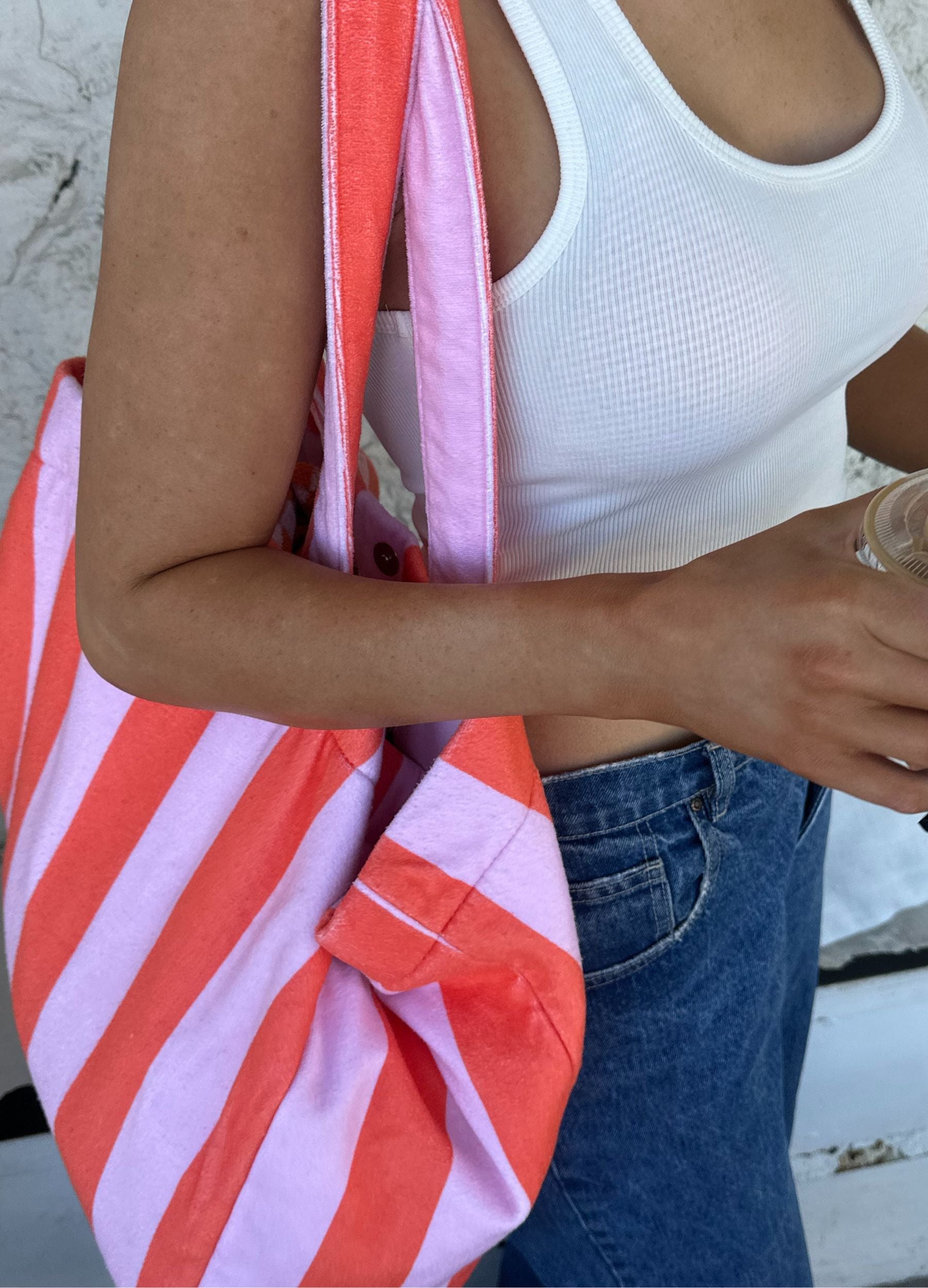 Person holding a orange and pink striped bag with a white top and blue jeans.