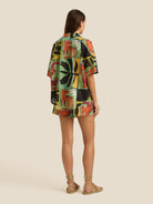 Woman wearing a colorful patterned shirt and shorts on a beige background