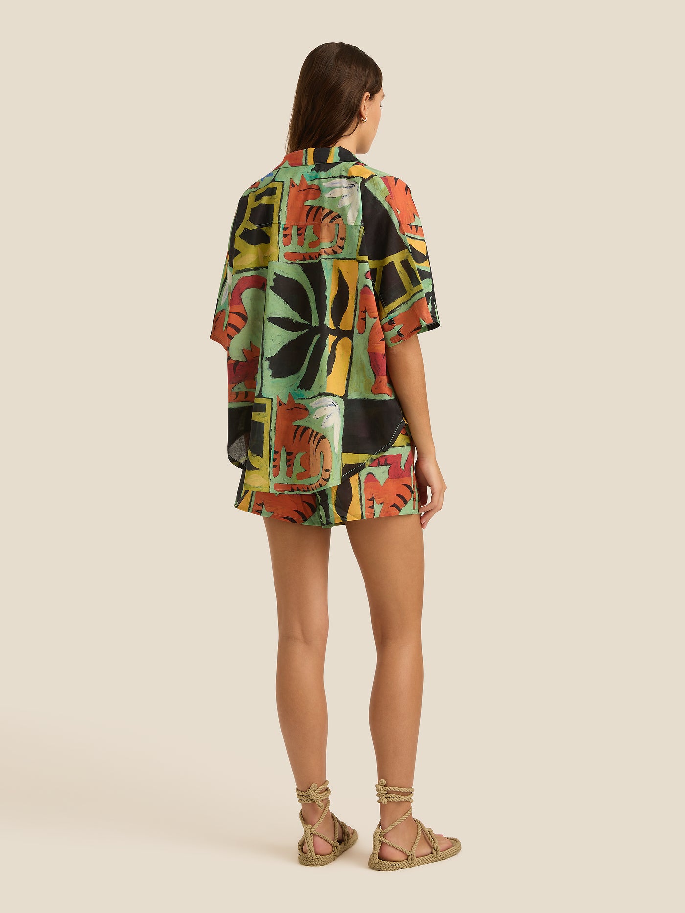 Woman wearing a colorful patterned shirt and shorts on a beige background