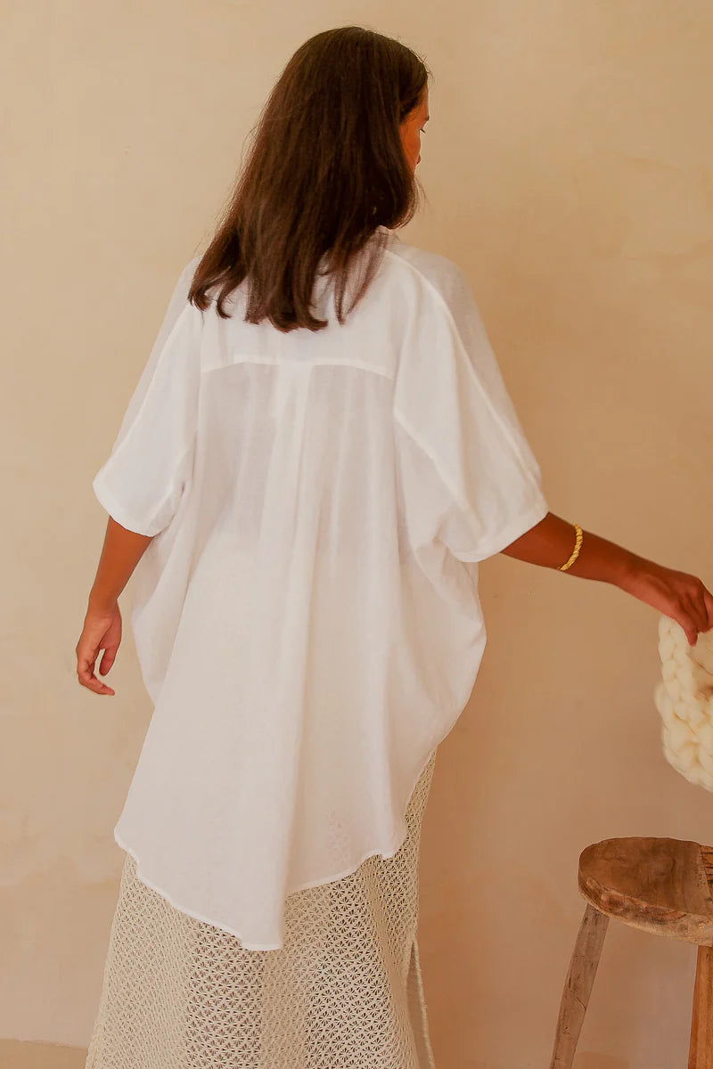 Woman wearing a white sheer top over a patterned skirt against a beige background