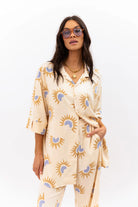 Woman wearing a cream-colored outfit with sun pattern on a white background