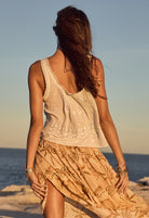 Woman in a beige dress standing on a beach with sunset in the background