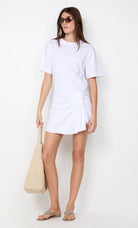 Woman wearing a white t-shirt dress holding a beige tote bag on a white background