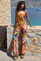 Woman in a colorful outfit standing against a stone wall with a scenic background