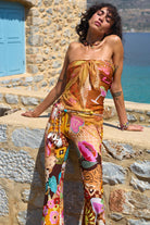 Woman wearing a colorful strapless dress with floral patterns against a stone wall and blue door background.