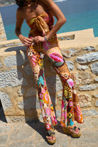 Person wearing colorful floral pants standing on a stone wall with a blue sea background