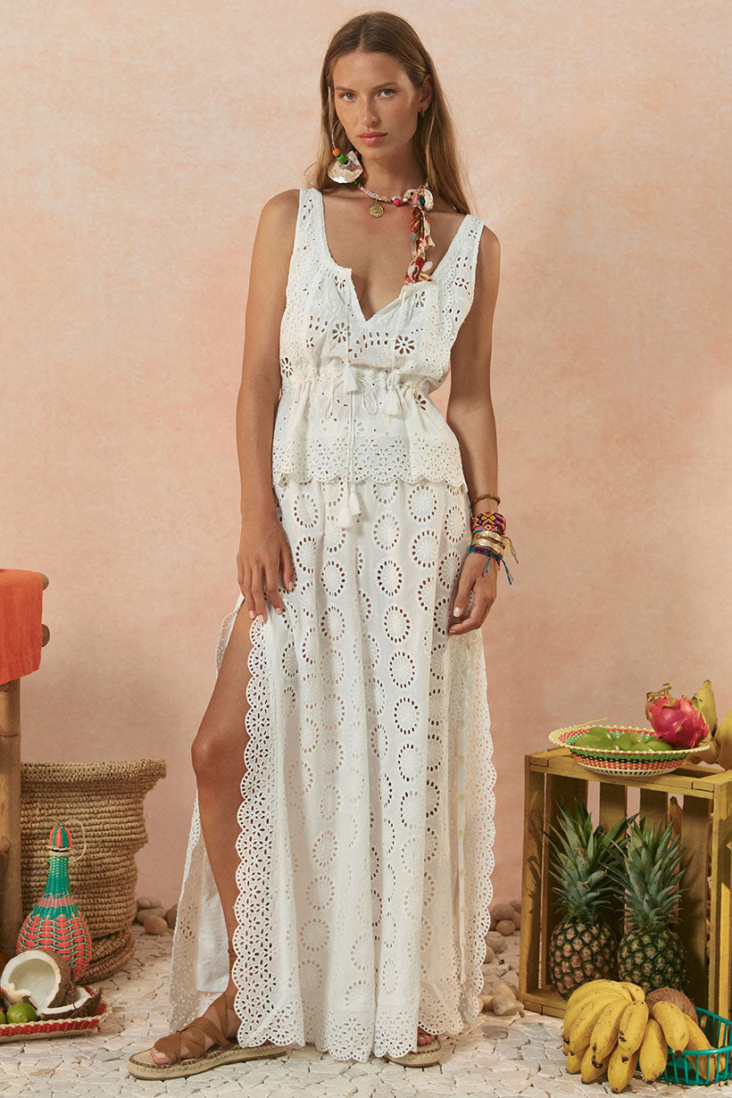 Woman wearing a white lace dress standing in a tropical setting with fruits and decor.