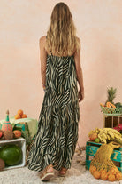 Woman in a zebra print dress standing in a room with fruits and vegetables on crates.