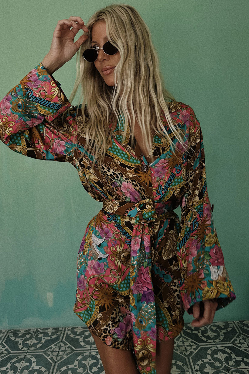 Person wearing a colorful patterned outfit with sunglasses against a green wall.