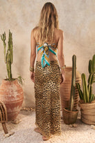 Woman in a leopard print dress with a blue ribbon standing among potted cacti.