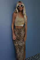 Woman wearing a crop top with a graphic design and leopard print pants against a blue wall.