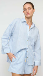 Woman wearing a blue and white striped shirt and shorts set against a plain background