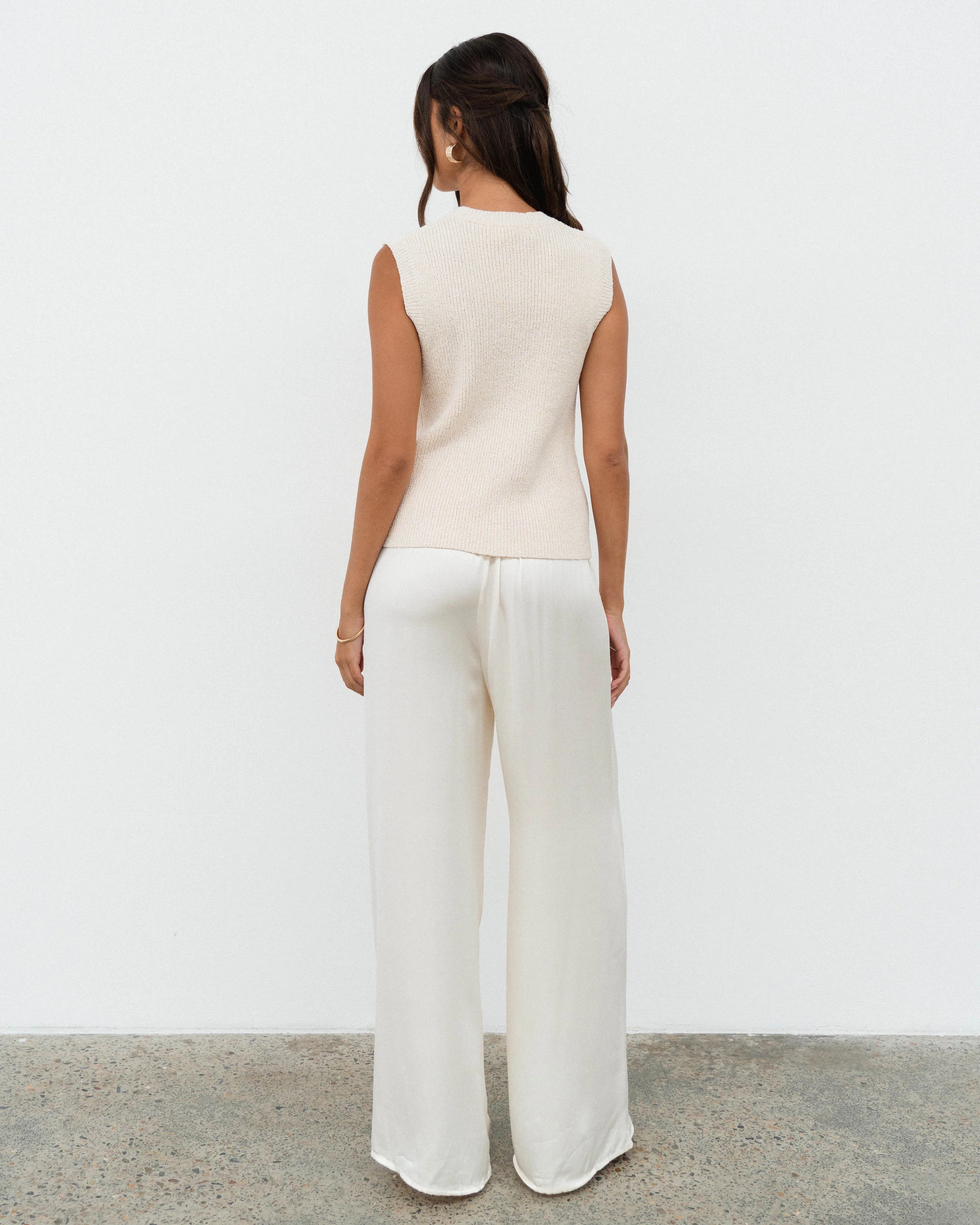 Woman wearing a white sleeveless top and wide-leg pants against a plain background