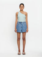 Woman wearing mint one shoulder tank and denim shorts