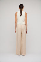 Person wearing a white sleeveless top and beige wide-leg pants on a light gray background