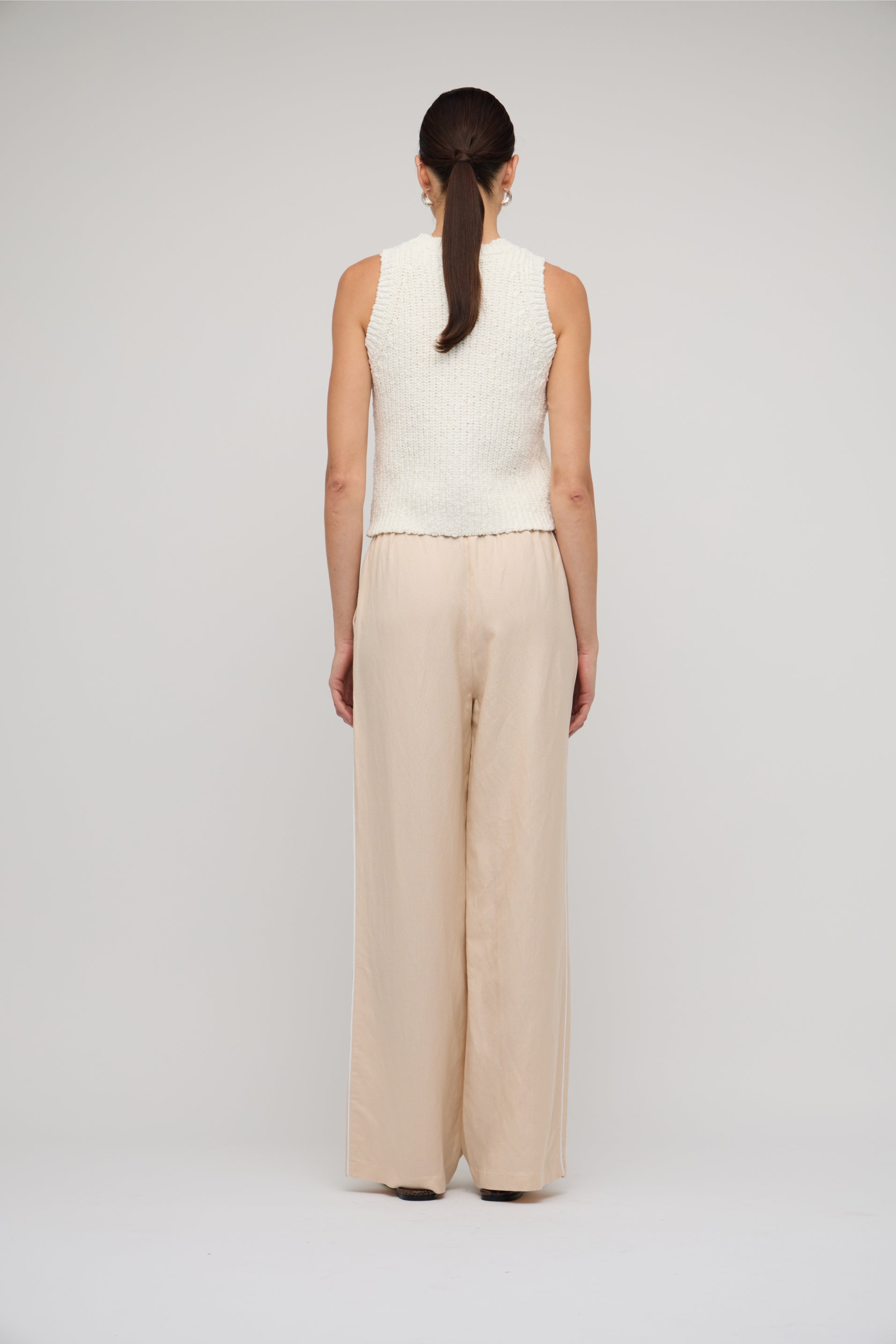 Person wearing a white sleeveless top and beige wide-leg pants on a light gray background