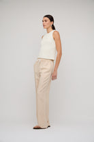 Woman wearing a white sleeveless top and beige pants on a plain background