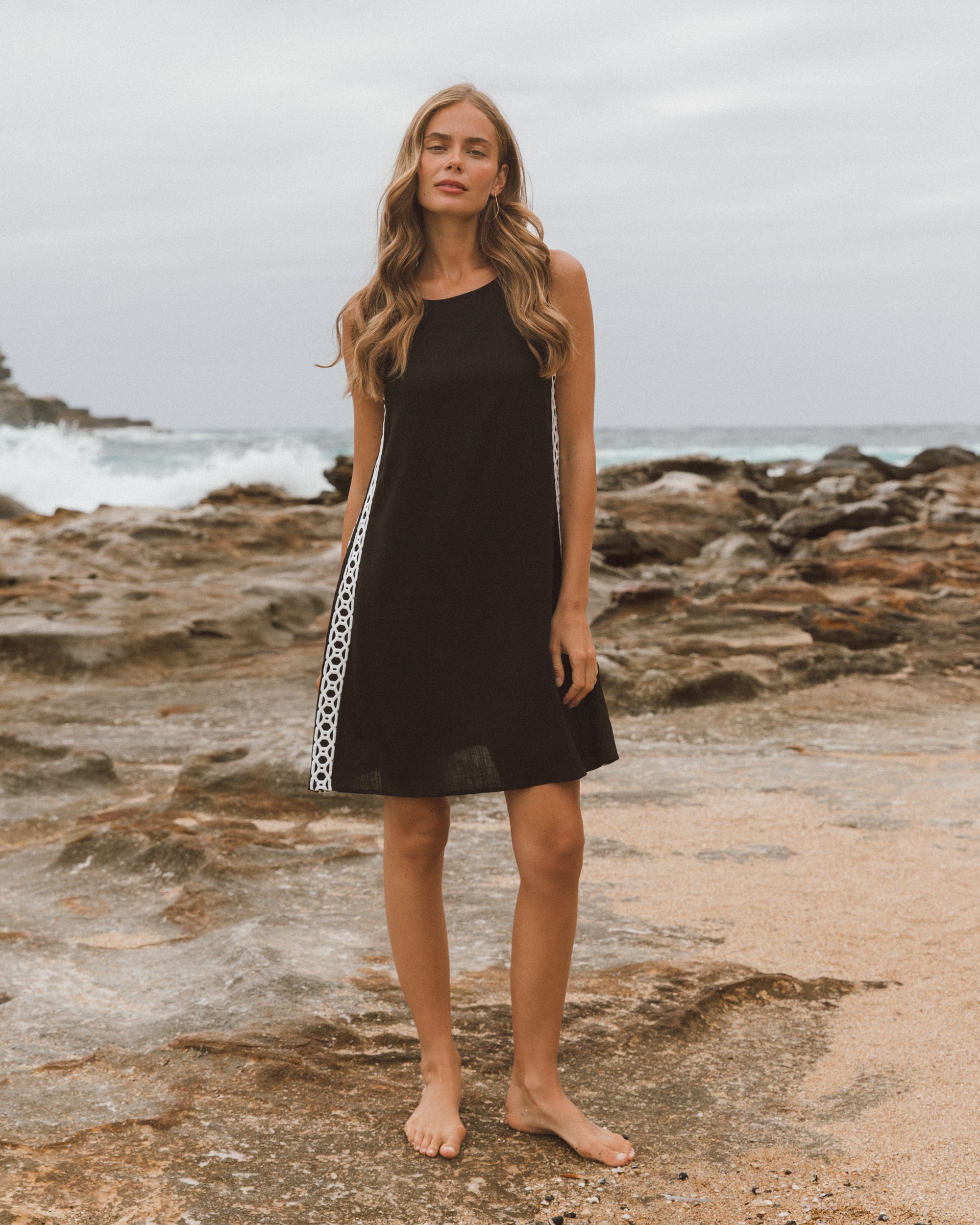 Woman wearing a black dress with a white stripe on a rocky beach.